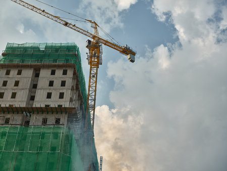 Construction site with a tall building and crane under a cloudy skyの写真素材