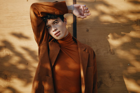 Stylish young man posing with a confident expression against a warm wooden background He wears a brown blazer and turtleneck sweater, showcasing a trendy autumn lookの写真素材