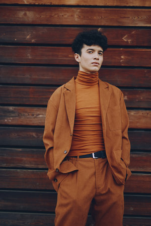 Stylish young man in an orange outfit standing against a wooden backgroundの写真素材