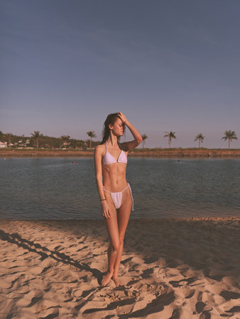 Woman in pink bikini standing on beach with palm trees in background on a sunny summer dayの写真素材