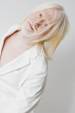Portrait of a person with long, light colored hair and a beard, wearing a white blazer against a clean, soft background, conveying a sense of elegance and artistryの写真素材