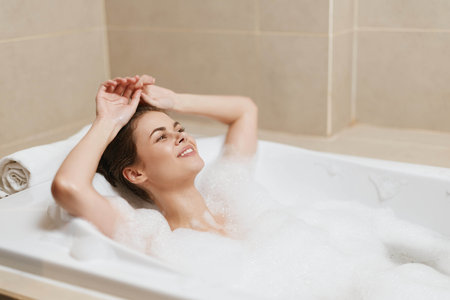 Relaxed young woman enjoying a bubble bath in a modern bathroom, smiling and feeling rejuvenated. Self-care and wellness concept at home.の写真素材