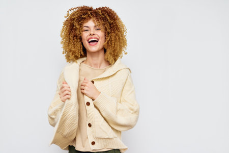 Smiling woman in cozy outfit with curly hair Warm tones and cheerful expression against a light, neutral background create an inviting atmosphere Perfect for fashion and wellness themesの写真素材