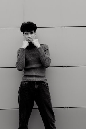 Young man in jeans and a sweater posing in front of a gray wall with hands on hipsの写真素材