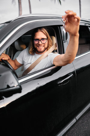 Smiling man in sunglasses driving a car and waving from the window