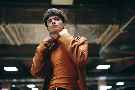 Portrait of a young man adjusting his collar in a modern urban setting The background features industrial elements with a metallic color schemeの写真素材