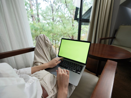 Young professional using a laptop in a cozy indoor setting, showcasing focus and creativity, with a green screen for design purposesの写真素材