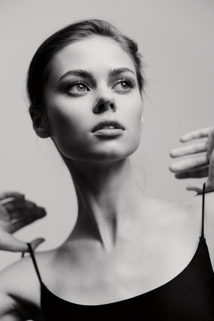 Elegant young woman with a graceful pose, showcasing confidence in a black outfit against a soft grayscale background. Portrait capturing beauty and poise.の写真素材