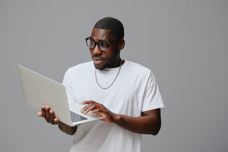 African model with laptop, casual wear, surprised expression, gray background, modern concept, technology, young adult, engaged in work or study, casual outfitの写真素材