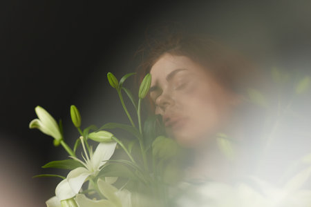 A serene young woman with curly hair surrounded by white lilies, conveying peace and tranquility in...