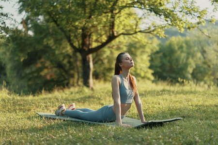 Woman practicing yoga in nature, demonstrating a cobra pose on a yoga mat in a serene outdoor...