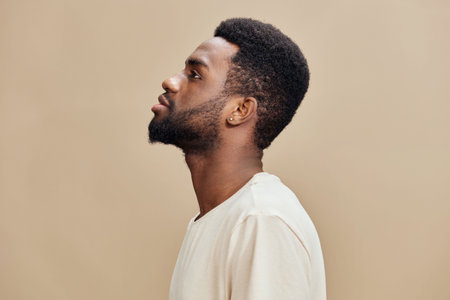 Profile portrait of a young Black man with a short beard, wearing a light shirt against a neutral background, showcasing a contemplative expression and minimalist styleの写真素材