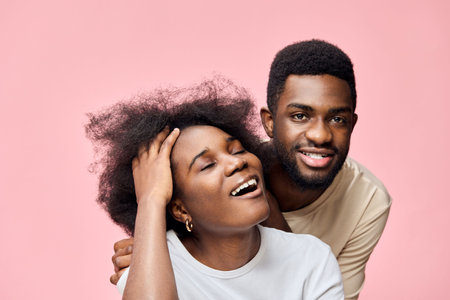 Happy couple with natural hair, smiling joyfully in front of a pink background, showcasing love and...