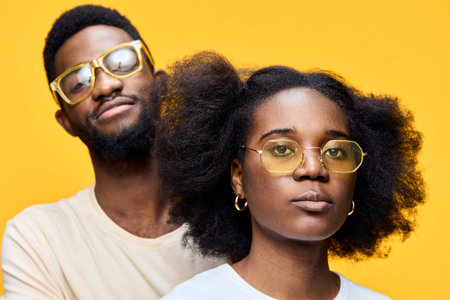Young Black couple with stylish eyewear, showcasing confidence and individuality against a vibrant yellow background, perfect for lifestyle and fashion themesの写真素材