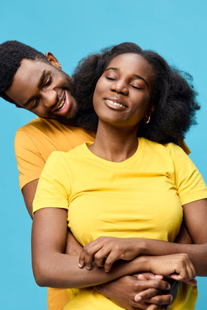 Joyful couple embracing with bright yellow shirts against a vibrant blue background, symbolizing love, happiness, and connection in a cheerful, warm atmosphereの写真素材