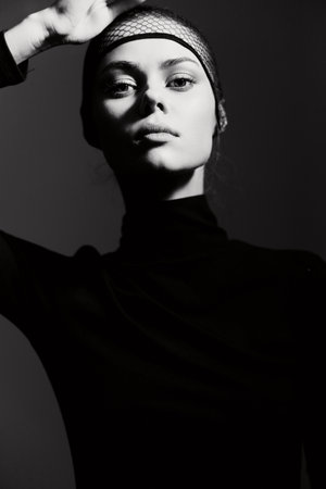 Elegant woman in black turtleneck posing confidently against a dark backdrop, showcasing fashion and beauty in monochrome. Strong and captivating expression.の写真素材
