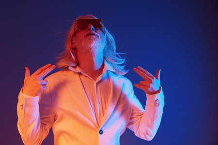 Stylish man in a white suit posing energetically against a vibrant blue and purple background,...