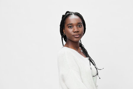 Confident young woman with braided hair, wearing a cozy white sweater, against a minimalistic white...