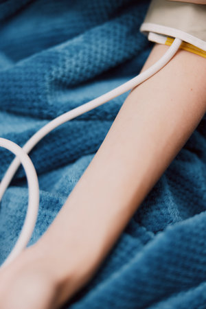Person laying in bed with a blood pressure monitor attached to their arm and a cuff on the other sideの写真素材