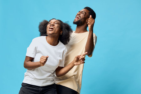 Happy diverse couple dancing joyfully against a bright blue background, showcasing vibrant emotions,...