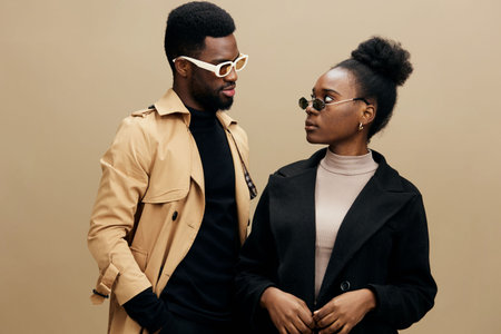 Stylish black couple wearing fashionable outfits and sunglasses, exuding confidence against a neutral beige background Perfect for showcasing modern fashion and accessoriesの写真素材