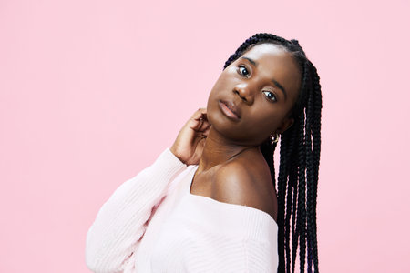 Portrait of a young Black woman with braided hair, wearing a soft pink off shoulder sweater, against...