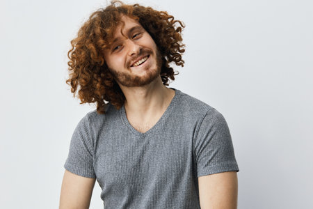Happy young man with curly hair smiling in casual gray shirt against a light background, showcasing...