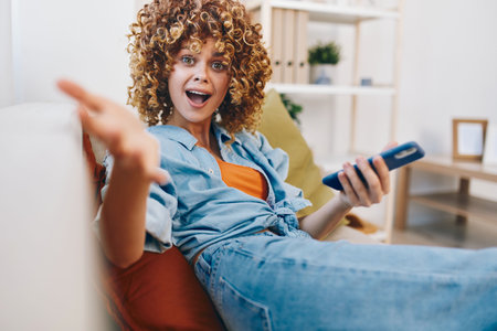 Smiling woman holding mobile phone, enjoying relaxation and entertainment on cozy sofa at home.