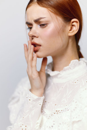 A thoughtful young woman with red hair in a white blouse expressing concern, showcasing emotions related to personal reflection and self awarenessの写真素材