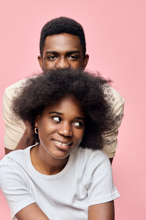 A joyful couple with natural hairstyle posing against a pink background, showcasing love,...