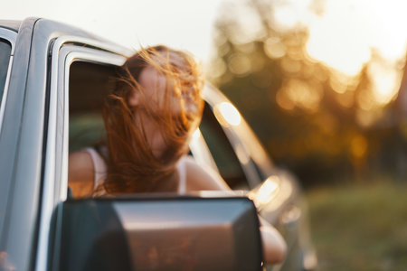 Young woman enjoying a road trip with wind in her hair, capturing the essence of freedom and adventure during sunset. Ideal for travel and lifestyle themes.の写真素材