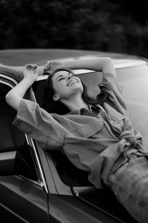 Young woman joyfully relaxing against a vintage car, wearing a casual outfit, with a happy...