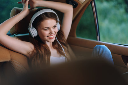 Young woman smiling with headphones in a car, enjoying music and relaxation in a natural green...