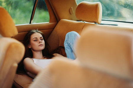 Young woman resting in a vintage car, wearing casual clothes, evoking a relaxed emotion in a natural green background, perfect for lifestyle and travel concepts.の写真素材