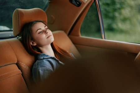 Relaxed young woman with long auburn hair lounging in a car, surrounded by a serene green background, evoking a sense of peace and tranquility.の写真素材