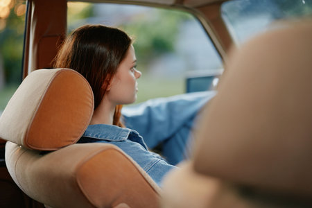 Young woman driving a vintage car, showcasing a relaxed and focused expression, dressed in a denim...