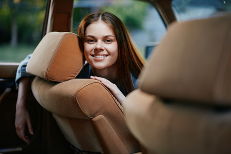 Young smiling female model with long hair sitting in car, showcasing joy and adventure in a warm, soft color palette, ideal for travel and lifestyle concepts.の写真素材
