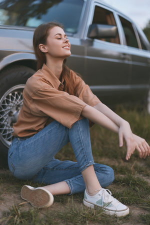 Young woman enjoying a sunny day outdoors, wearing casual denim and a brown shirt, sitting beside a...