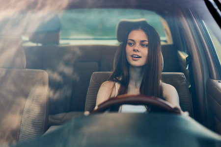 Young woman enjoying a drive in a car, smiling with confidence, showcasing a casual outfit against a...