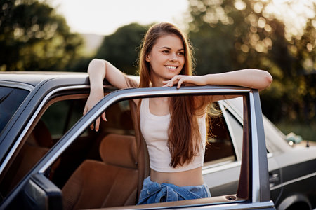 Smiling young woman with long hair leaning out of a vintage car, dressed casually, depicting freedom...