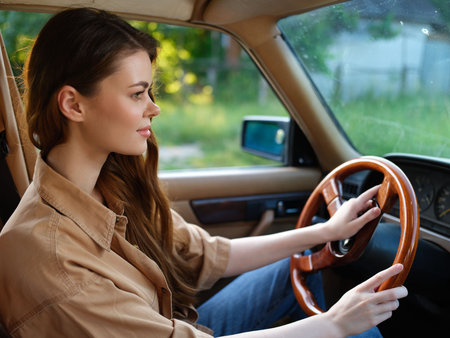 Young woman driving an old-fashioned car in a natural setting, showcasing confidence and tranquility, wearing a casual beige shirt, reflecting a vintage aesthetic.の写真素材