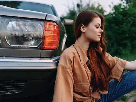 Young woman with long hair in casual attire sitting beside a vintage car, exuding a stylish and...