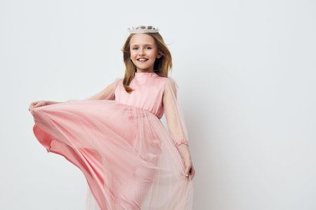 A joyful young girl wearing a pink dress and a crown, smiling and playfully twirling, ideal for concepts of childhood, fashion, and celebrationの写真素材