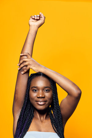 Smiling woman with braided hair posing against a vibrant yellow background, showcasing confidence and joy in a stylish outfitの写真素材