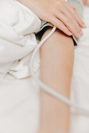 Person in bed with blood pressure cuff on arm and white sheet covering up to neckの写真素材