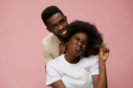 Young African couple enjoying a playful moment against a soft pink background, showcasing vibrant emotions and diverse styles, perfect for joyful lifestyle themesの写真素材