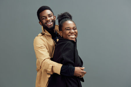 Happy African couple smiling together, enjoying a joyful moment in stylish outfits against a neutral gray background, showcasing love and connectionの写真素材