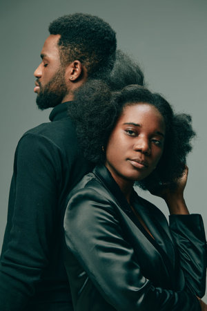 Two stylish models exuding confidence, showcasing natural hair, with contrasting black attire, against a muted gray backgroundの写真素材