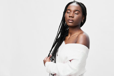 Young woman with braided hair in a white sweater, serene expression, emphasizing confidence and style against a minimalist white backgroundの写真素材