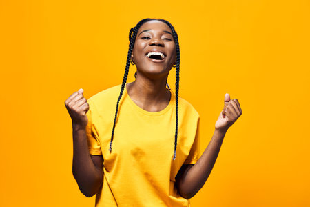 Joyful young woman celebrating success in a bright yellow t shirt against a vibrant yellow...